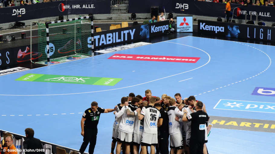 Handball Team steht zur Besprechung im Kreis auf dem Spielfeld